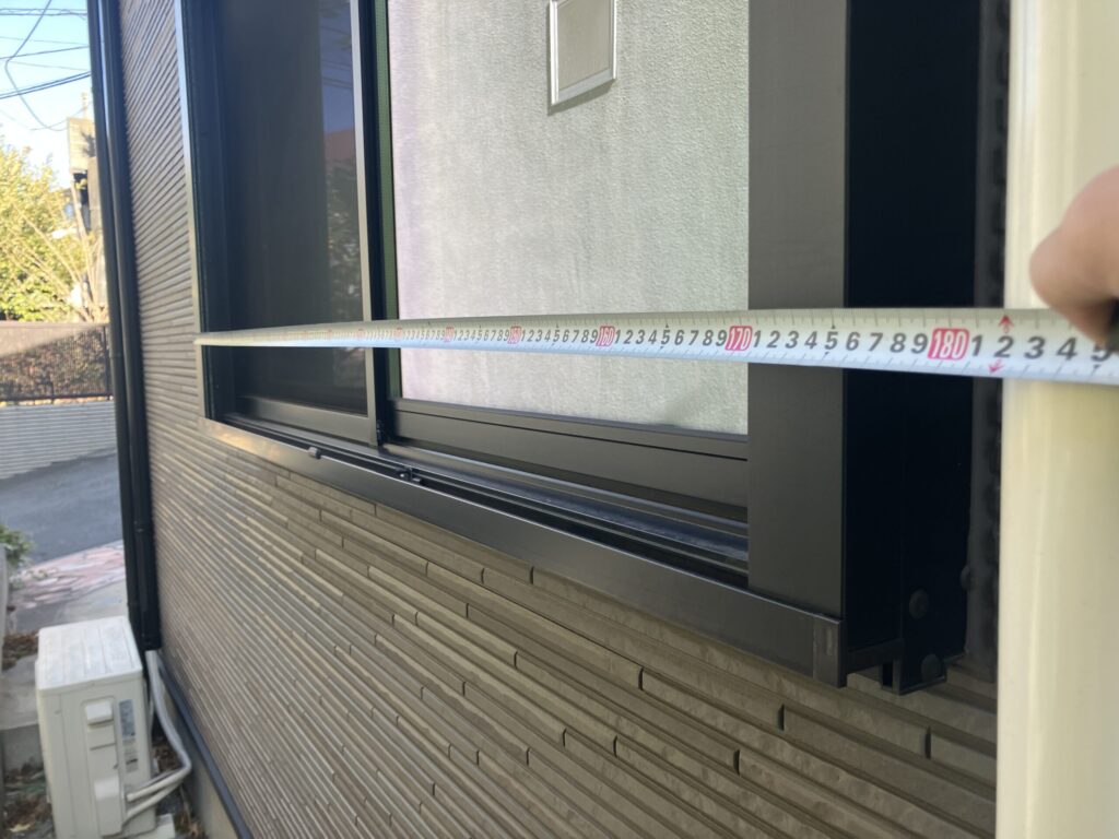 外壁サイディング住宅のサッシ廻りコーキングをメジャーで横方向に測っている様子