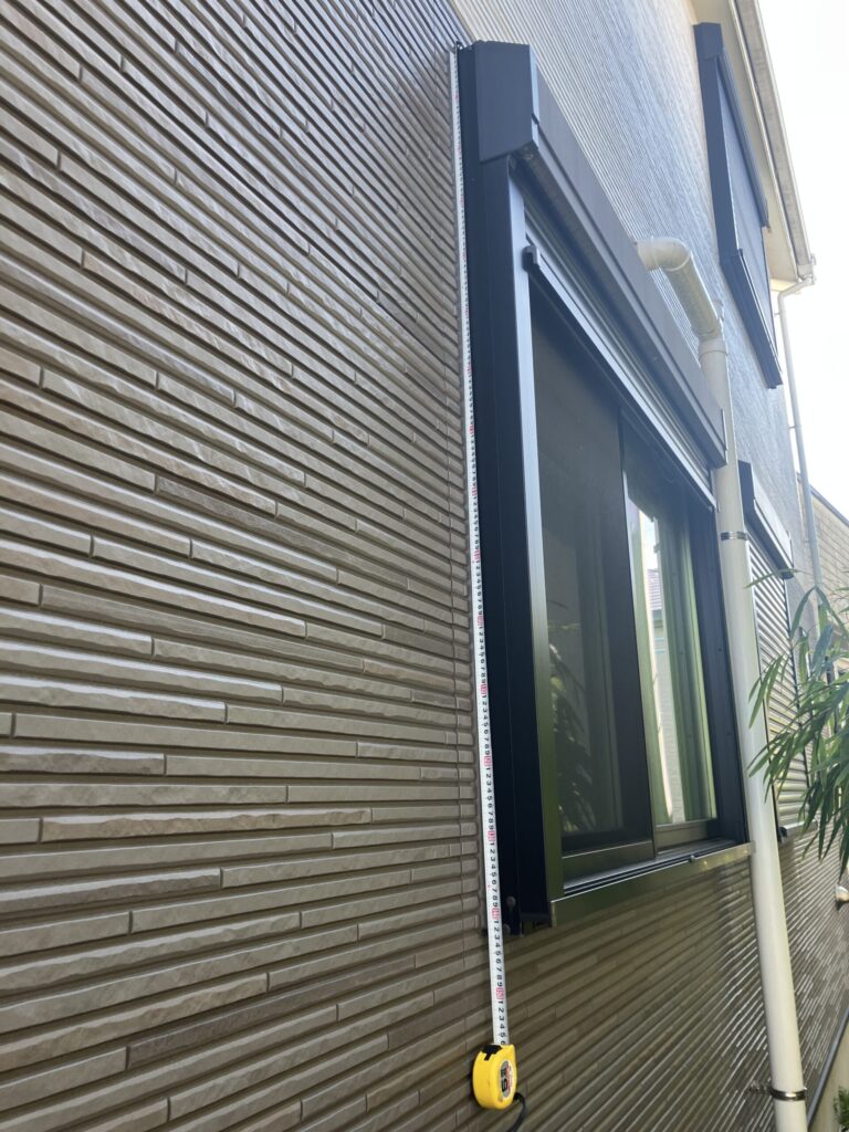 サイディング外壁のサッシ縦方向コーキング長さをメジャーで測っている様子