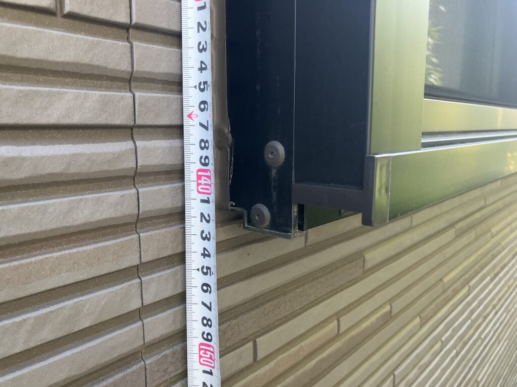 サッシ縦枠のコーキング長さをメジャーで測定しているアップ写真